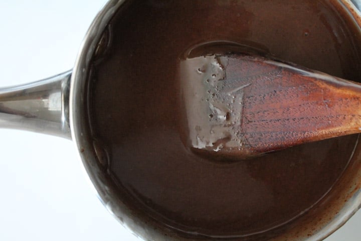 saucepan with dark chocolate being stirred by a wooden spoon