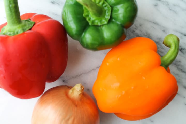 bell peppers and on onion on a marble counter