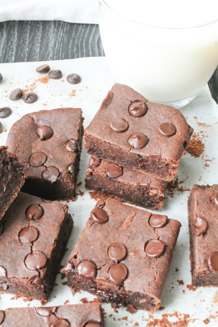 Black bean brownies on parchment paper with a frosty glass of milk in the background