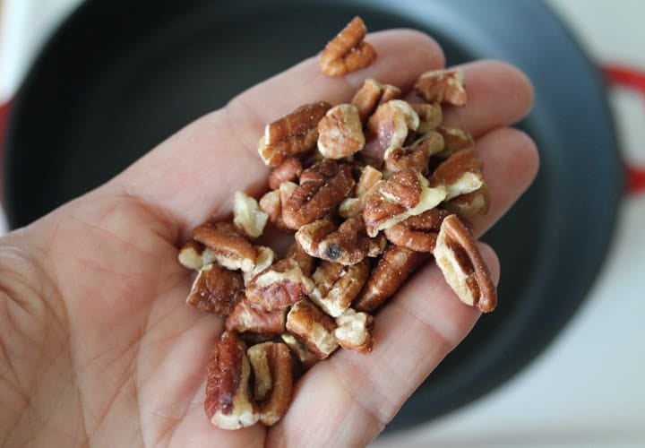 A hand holding toasted pecans
