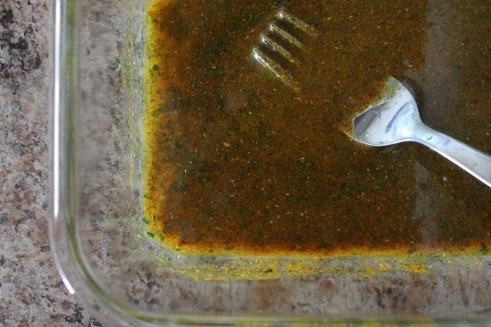 A fork stirring Coconut Curry Chicken marinade in a glass pyrex dish