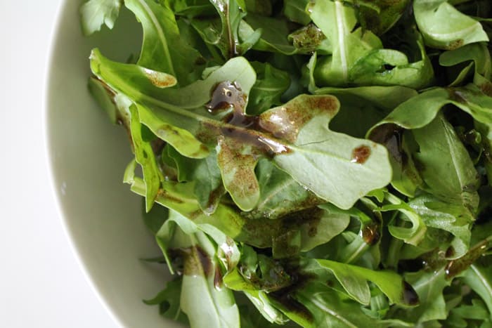 arugula leaves in a bowl being dressed with balsamic glaze dressing