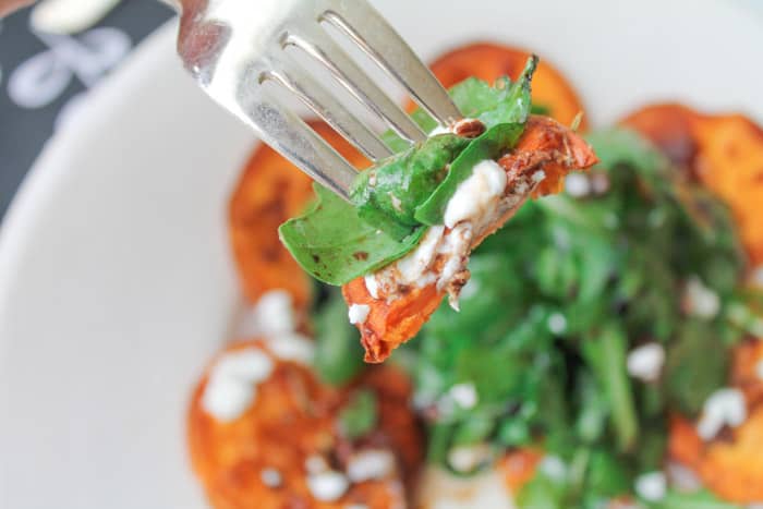 a fork with a bite of arugula salad, sweet potato and goat cheese