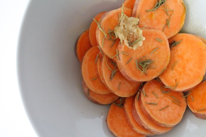 sliced rounds of sweet potatoes in a mixing bowl being coated in olive oil
