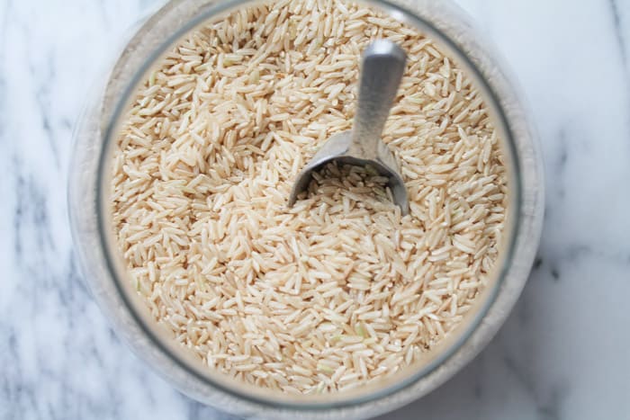 Brown rice in a glass storage jar on a white marble counter