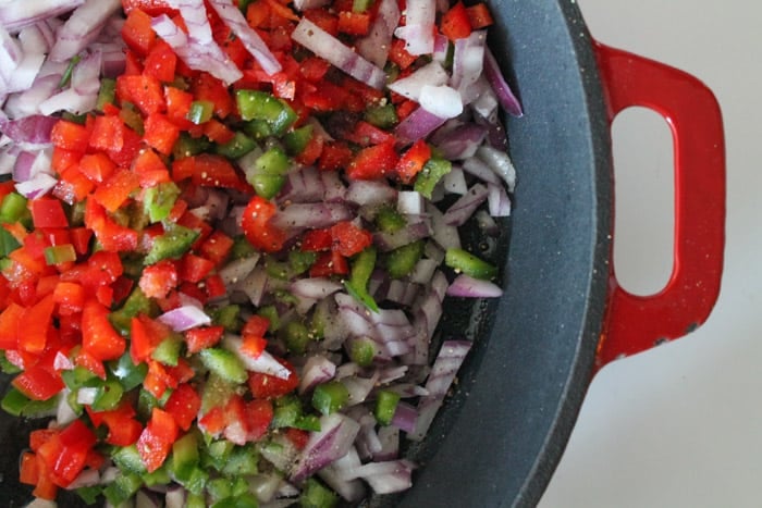 chopped peppers and onions sauteing in a cast iron skillet.