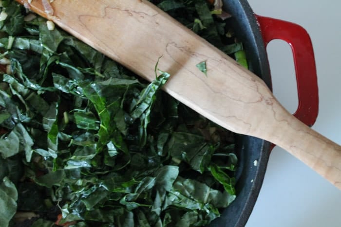 chopped kale being stirred in a large skillet.