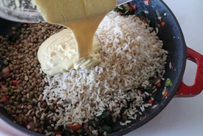 lemon tahini dressing being poured over cooked brown rice and lentils in a large cast iron skillet.