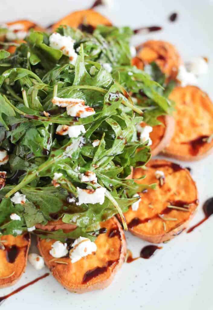 arugula salad topped with crumbled goat cheese served on top of roasted sweet potatoes and drizzled with balsamic glaze