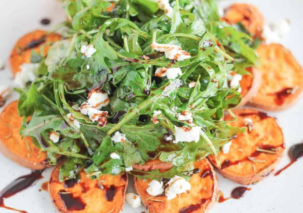 arugula salad topped with crumbled goat cheese served on top of roasted sweet potatoes and drizzled with balsamic glaze