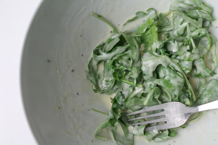 Arugula being tossed with lemon and goat cheese