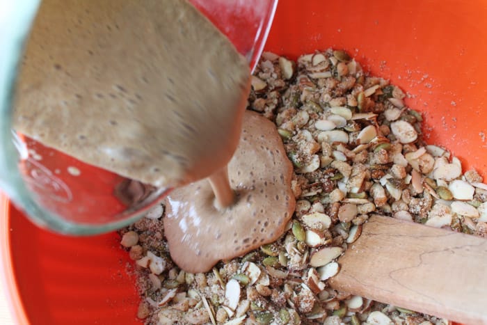 Sugar free granola ingredients in an orange mixing bowl with a banana mixture being poured overtop