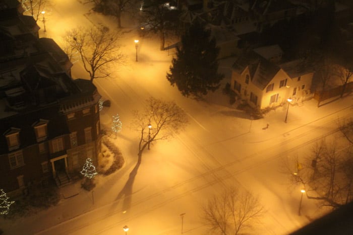 a snow covered street with soft light from lamp posts.