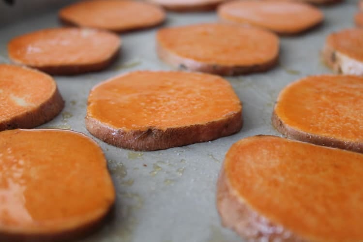 sliced sweet potatoes lined up on a parchment lined baking sheet ready for the oven
