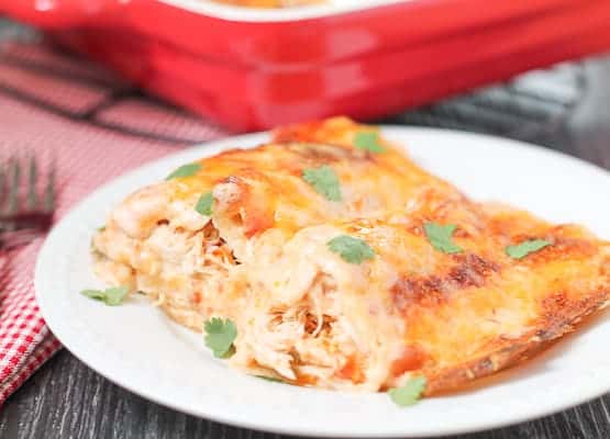 Chicken Enchiladas on a white plate with a red casserole dish and red checkered napkin in the background