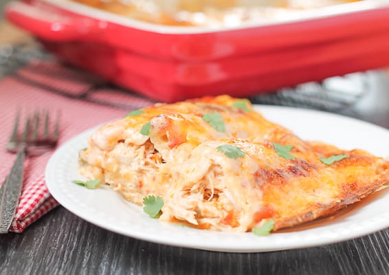 Chicken Enchiladas on a white plate with a red casserole dish and red checkered napkin in the background