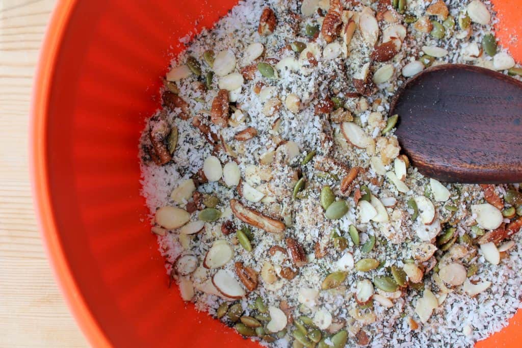 a bowl with nuts and seeds being stirred with a wooden spoon