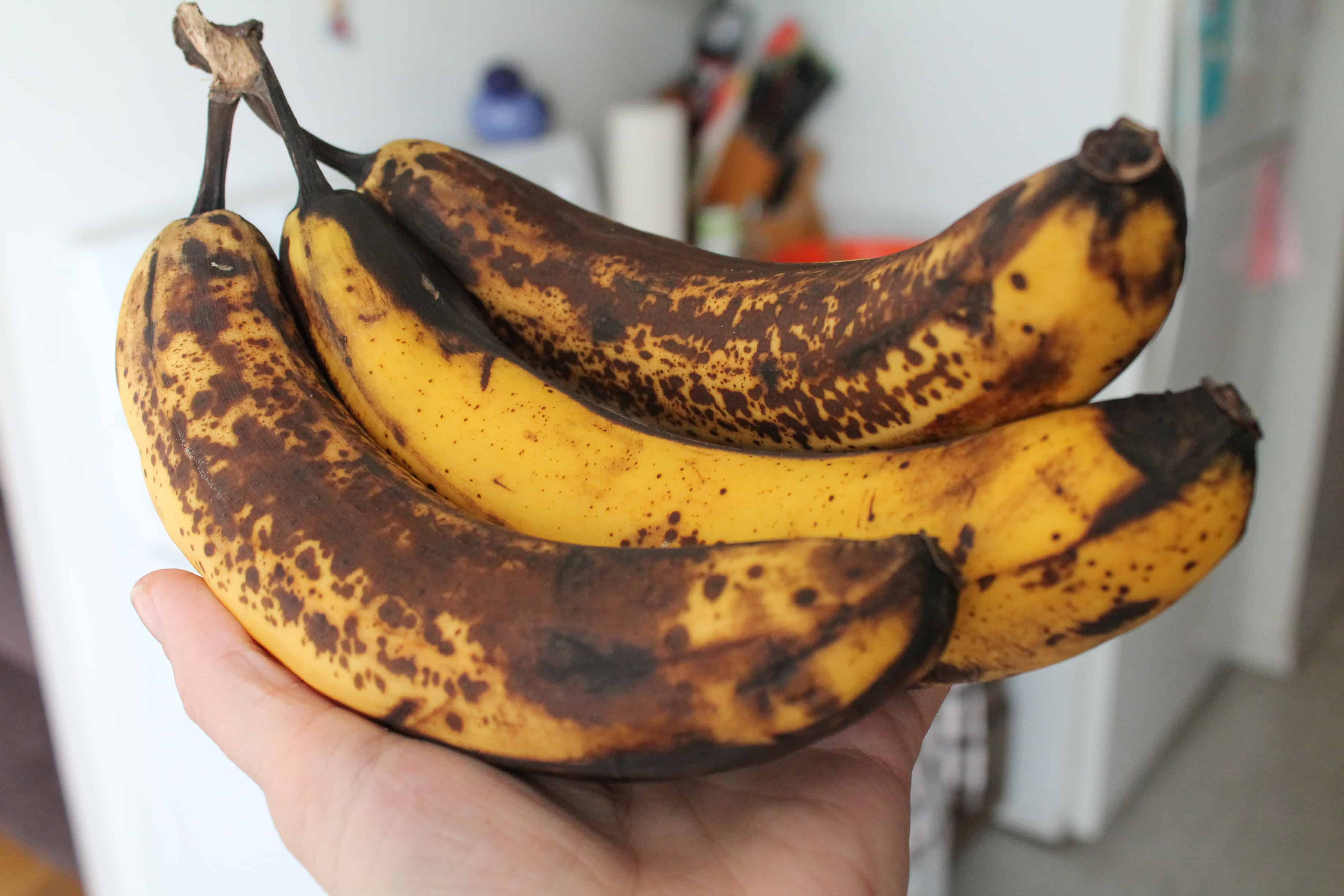 a hand holding a bunch of brown bananas