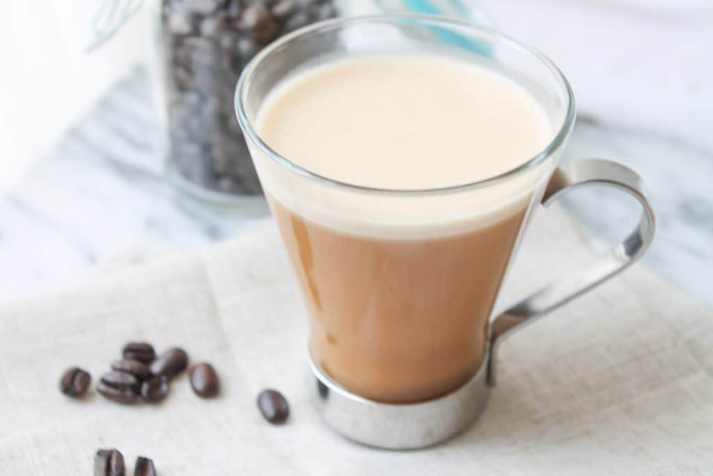 Creamy coffee in a glass mug with coffee beans in the background