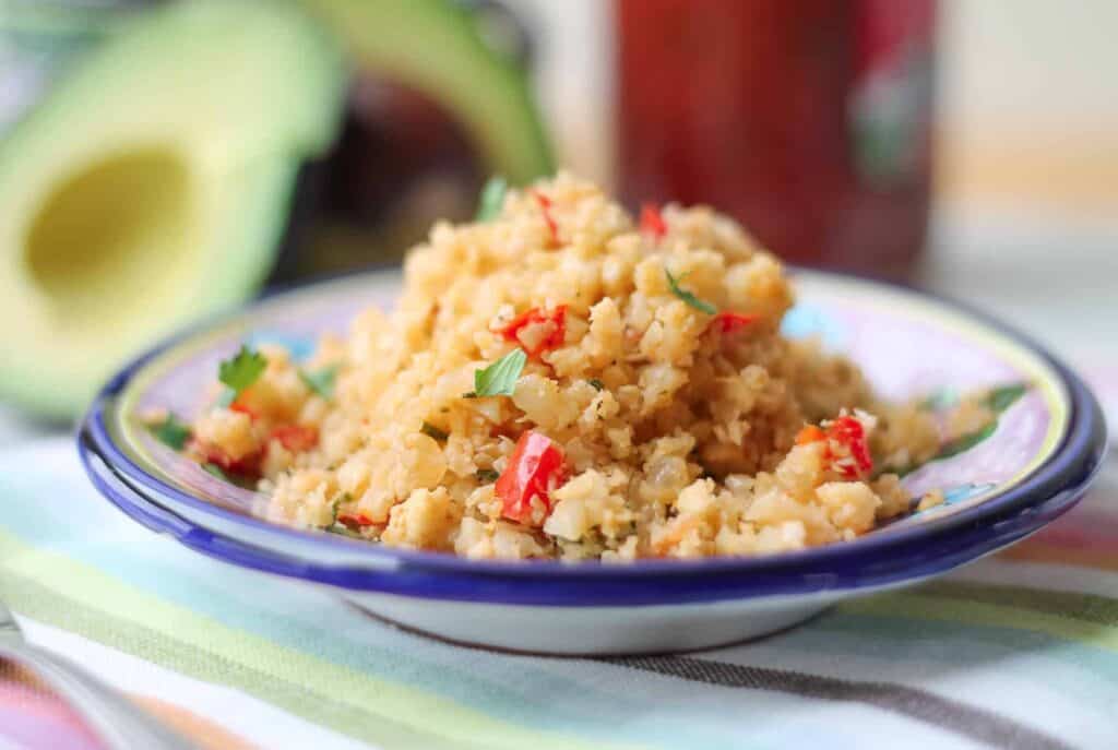 Paleo cauliflower side dish on a painted ceramic dish with fresh avocado in the background