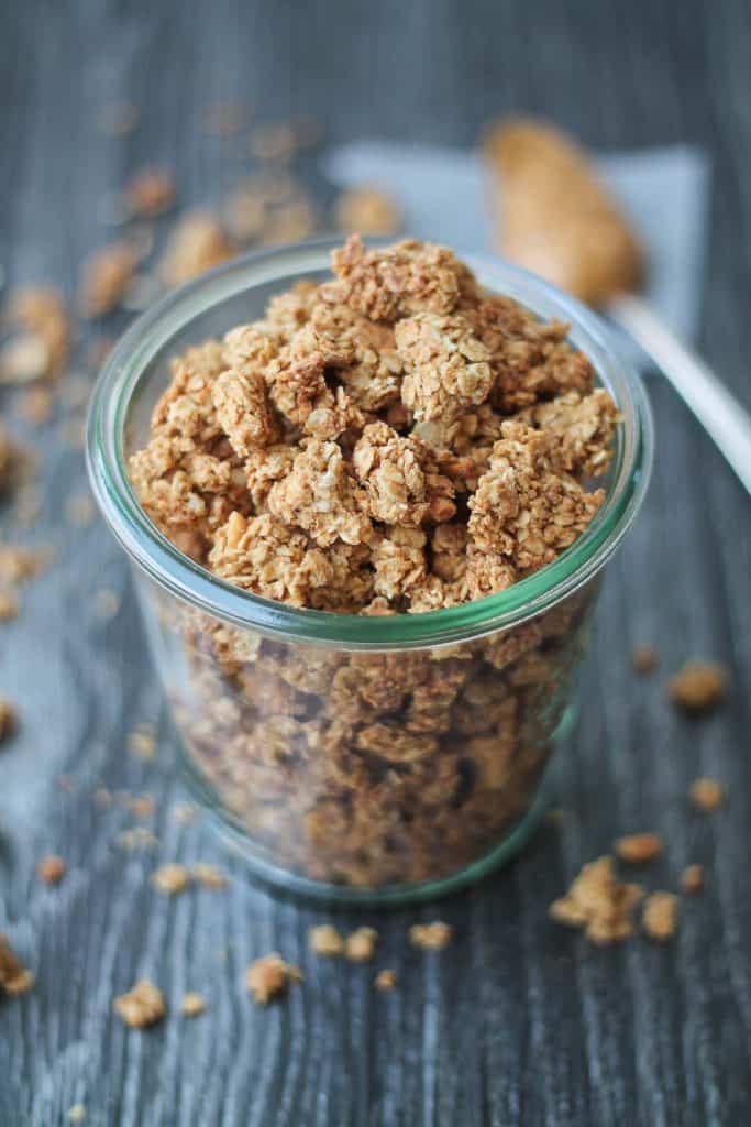 Peanut Butter Granola in glass jar with a spoonful of peanut butter in the background