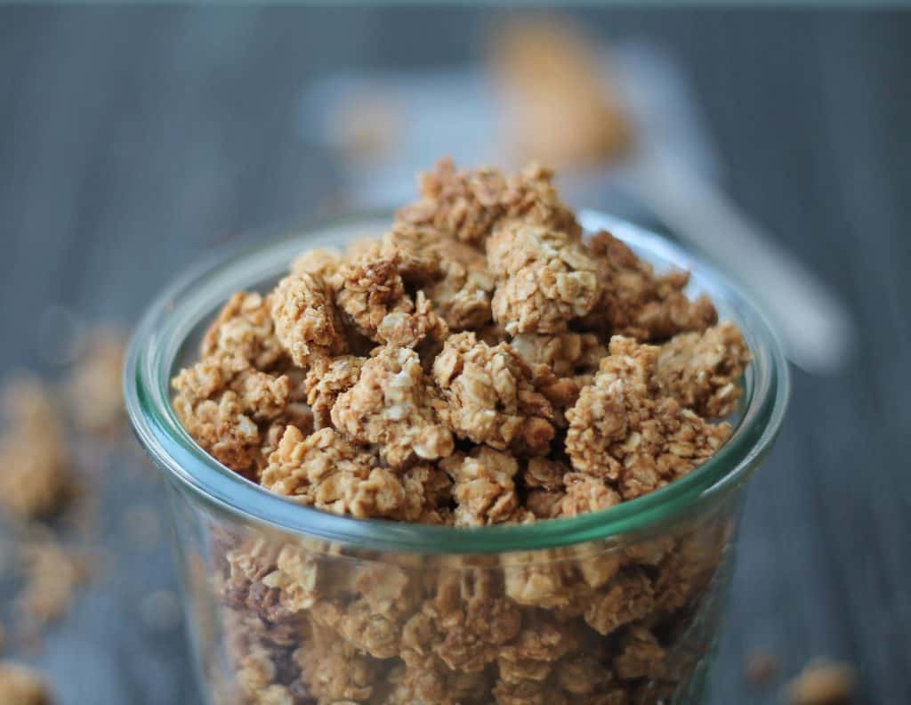 Peanut Butter Granola in glass jar with a spoonful of peanut butter in the background