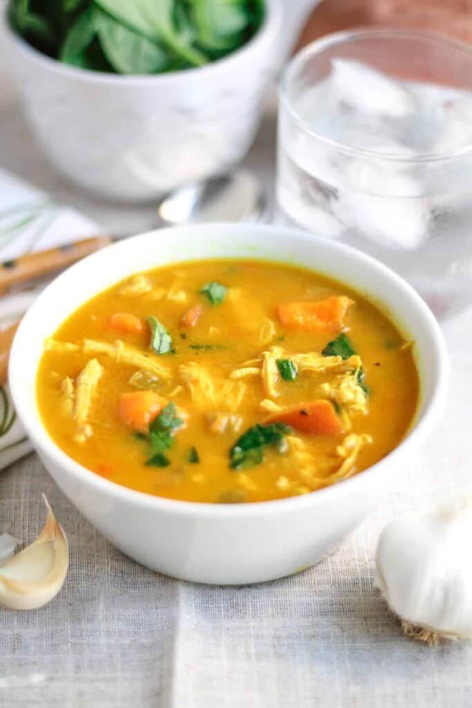 Creamy Coconut Curry Chicken Vegetable Soup in a white bowl on a linen tablecloth with a bowl of salad and a water glass in the background