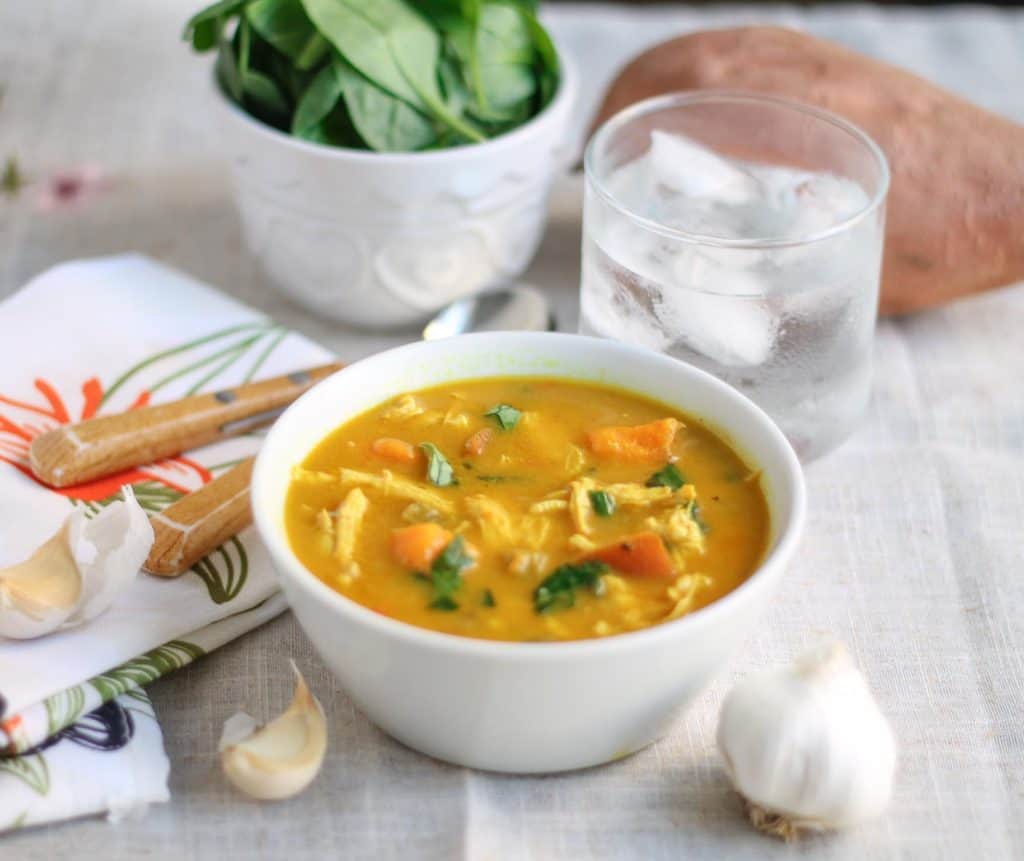 Creamy Coconut Curry Chicken Vegetable Soup in a white bowl on a linen tablecloth with a bowl of salad and a water glass in the background