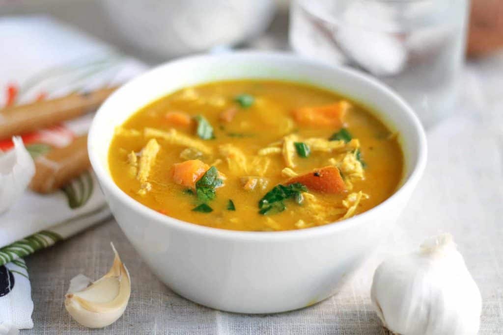 Creamy Coconut Curry Chicken Vegetable Soup in a white bowl on a linen tablecloth with a bowl of salad and a water glass in the background