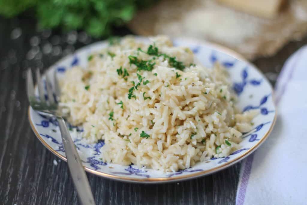 Brwon rice sprinkled with fresh chopped parsley on a blue patterned plate with gold trim on a dark wood background