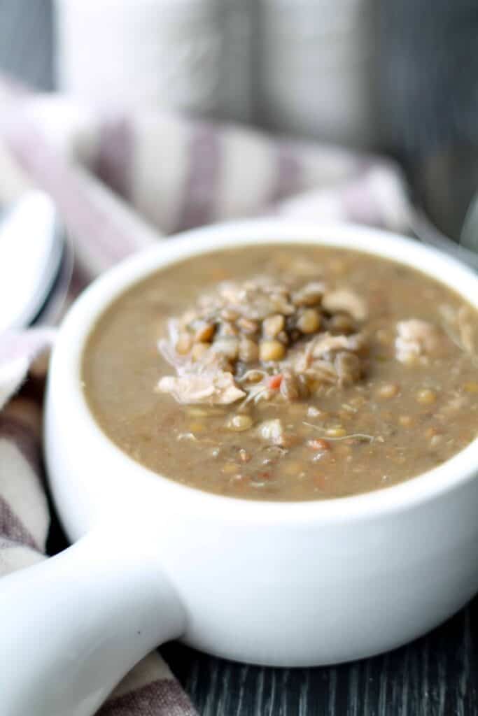 Instant Pot Chicken Lentil Soup in a white crockery bowl with a soft striped napkin in the background