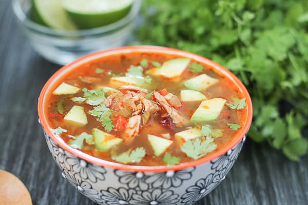 Chipotle Lime Chicken Soup in a bowl with fresh greens and lime in the background