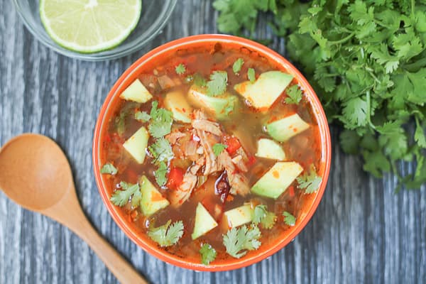 Chipotle Lime Chicken Soup in a bowl with fresh greens and lime in the background