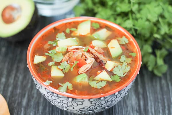 Chipotle Lime Chicken Soup in a bowl with fresh avocado in the background