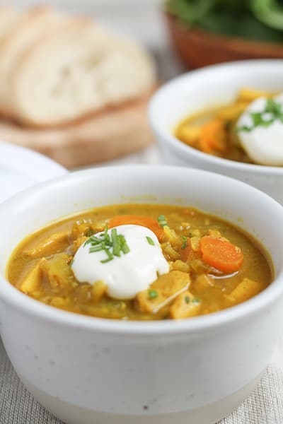 Gluten Free Brown Rice Mulligatawny in a white bowl with sliced bread and salad in the background