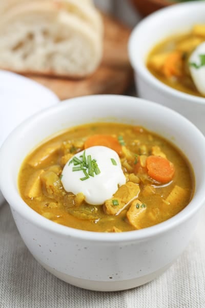 Brown Rice Mulligatawny Soup in a white bowl topped with a dollop of sour cream