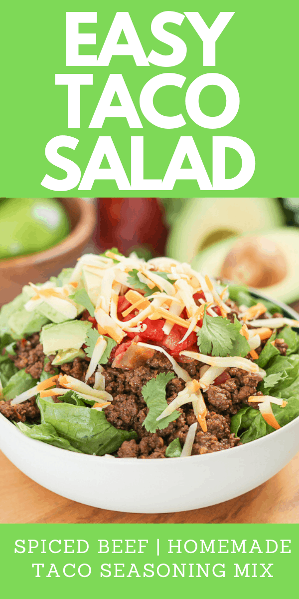 salad topped with spiced beef and shredded cheese with a bowl of fres limes and avocacdo in the background