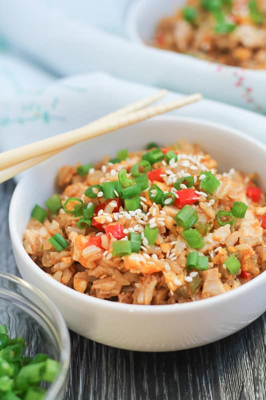 Chicken Fried Brown Rice in white bowls with chopsticks and sliced green onions in the background.