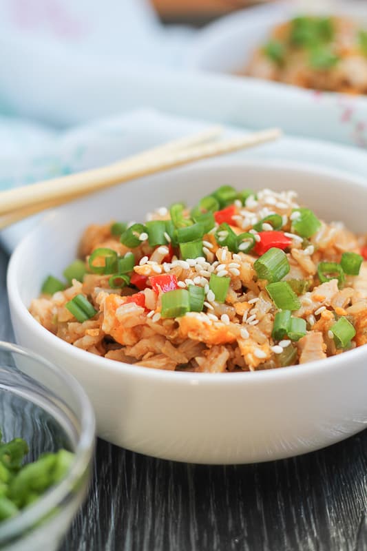 Chicken Fried Brown Rice in white bowls with chopsticks and sliced green onions in the background.