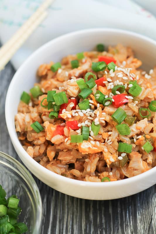 Chicken Fried Brown Rice in white bowls with chopsticks and sliced green onions in the background.