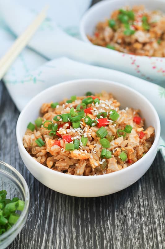 Chicken Fried Brown Rice in white bowls with chopsticks and sliced green onions in the background.