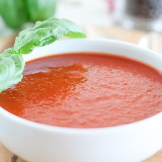 a bowl of roasted tomato basil soup with fresh basil leaves in the background