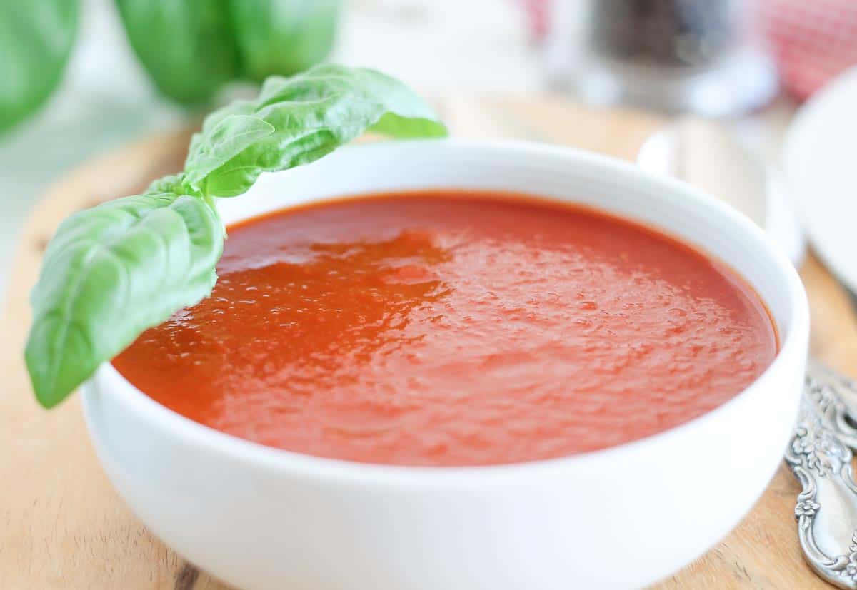 a bowl of roasted tomato basil soup with fresh basil leaves in the background