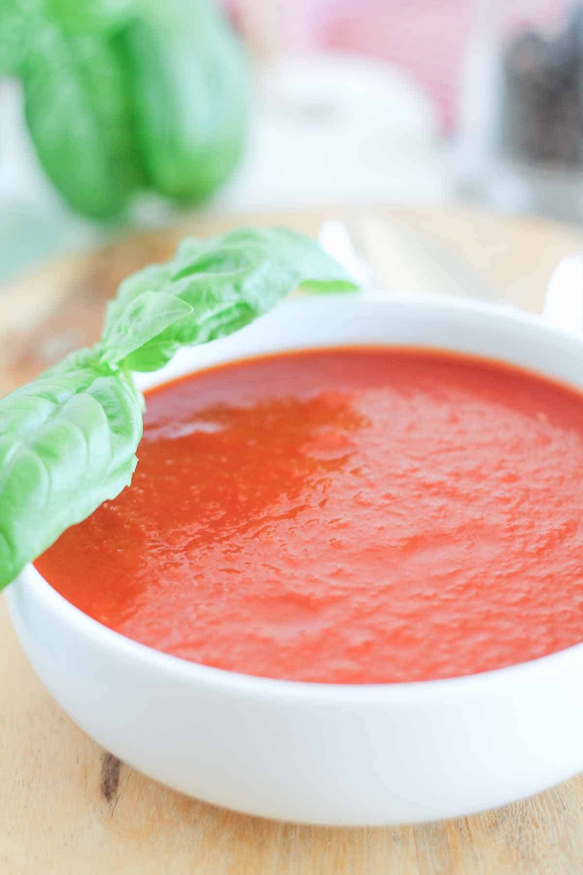 a bowl of roasted tomato basil soup with fresh basil leaves in the background