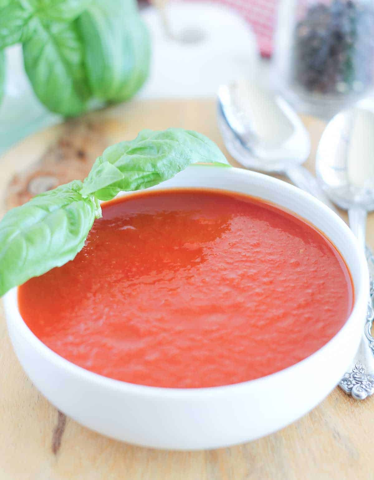 a bowl of roasted tomato basil soup with fresh basil leaves in the background