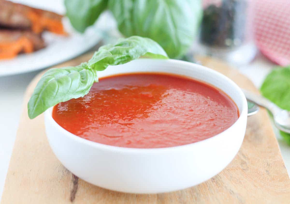 a bowl of roasted tomato basil soup with a grilled cheese sandwich in the background
