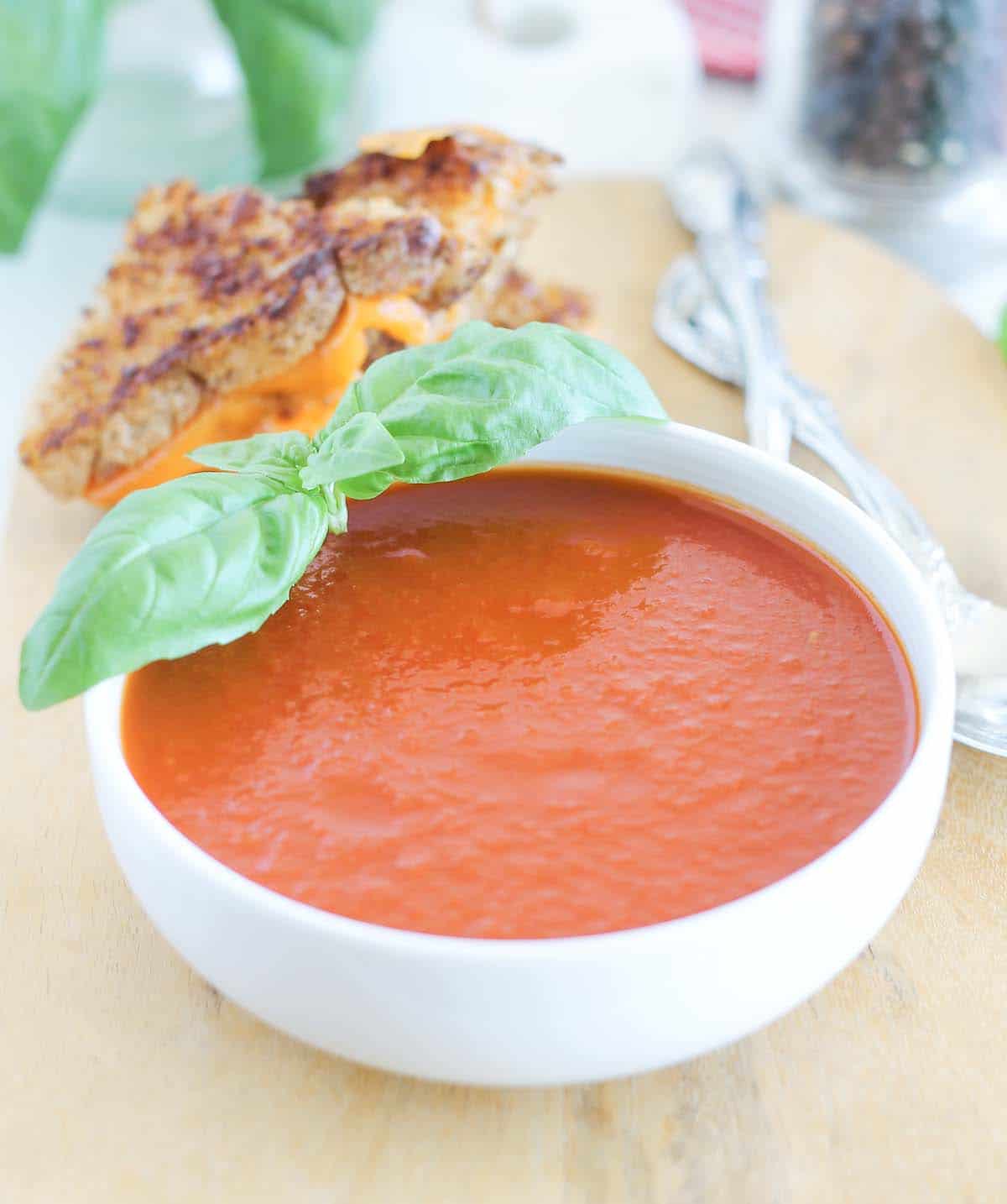 a bowl of roasted tomato basil soup with a grilled cheese sandwich in the background