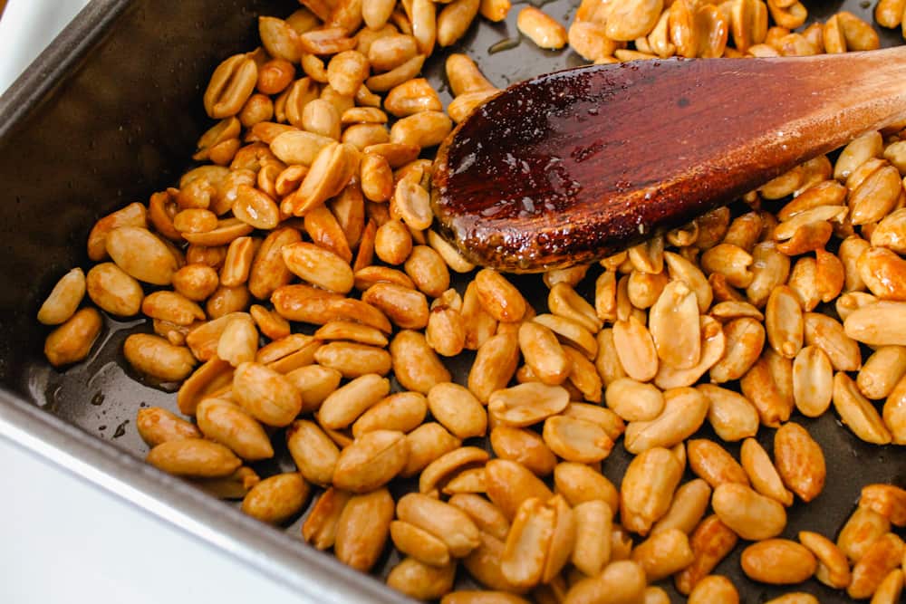 a spoon stirring nuts in a baking pan.