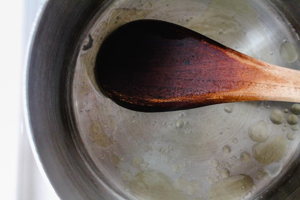a spoon stirring coconut oil and honey in a small saucepan.