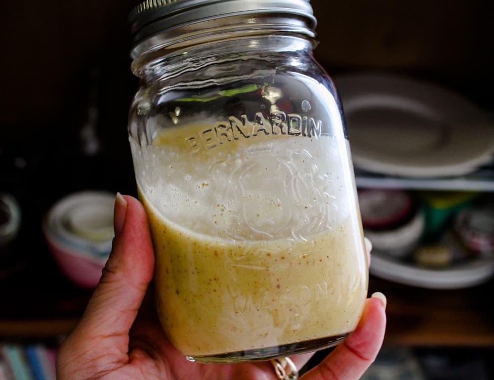 a hand holding a jar of honey mustard dressing